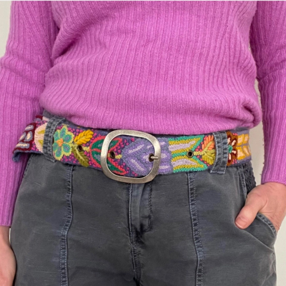 Person wearing a colorful embroidered belt with a purple sweater and gray pants.