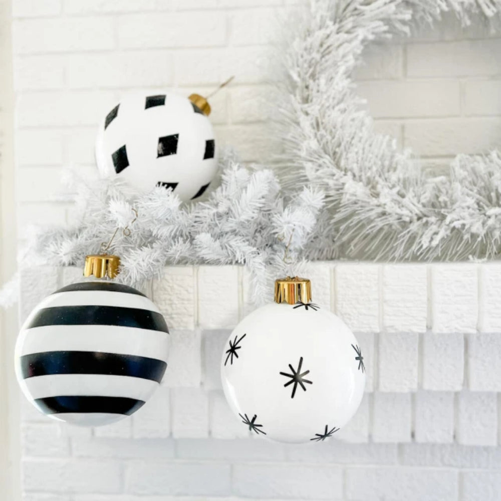 Black and white Christmas ornaments on a white tree with a white brick wall background.