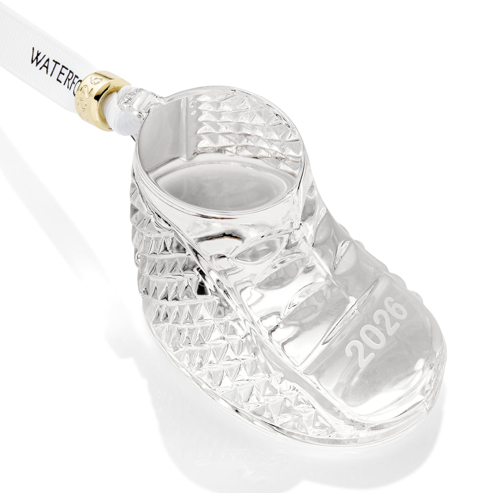 Clear glass baby boot with '2026' printed on it, attached to a white ribbon with "Waterford" on it