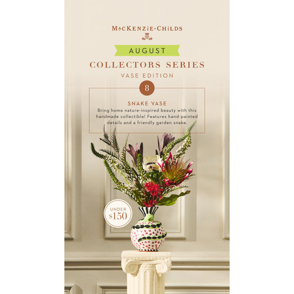 A promotional product card for the McKenzie-Childs August Collectors Series Vase Edition, featuring a hand-painted snake vase filled with green foliage and red flowers, displayed on a pedestal against an elegant cream-colored wall background.