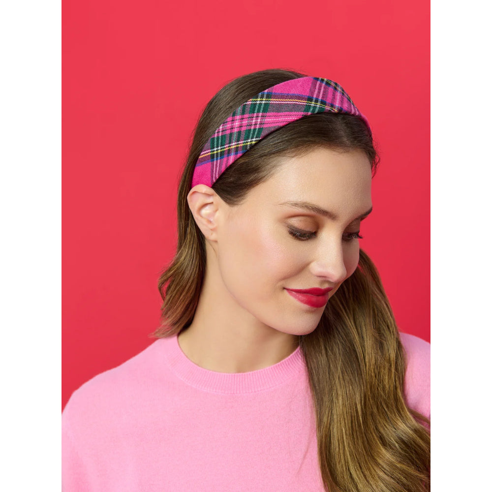 A woman wearing a pink and green plaid headband, posing against a solid red background.
