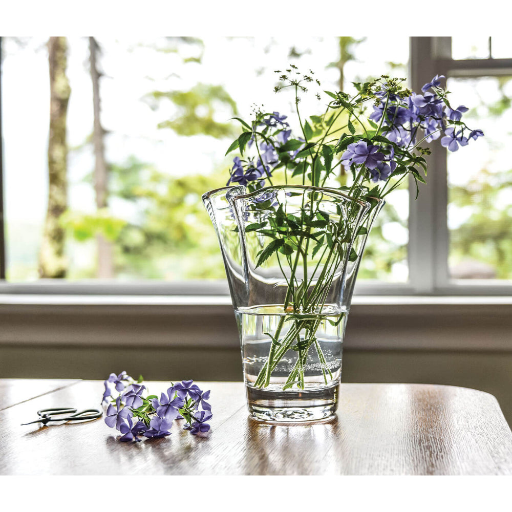 Clear vase with purple flowers on a wooden table by a window