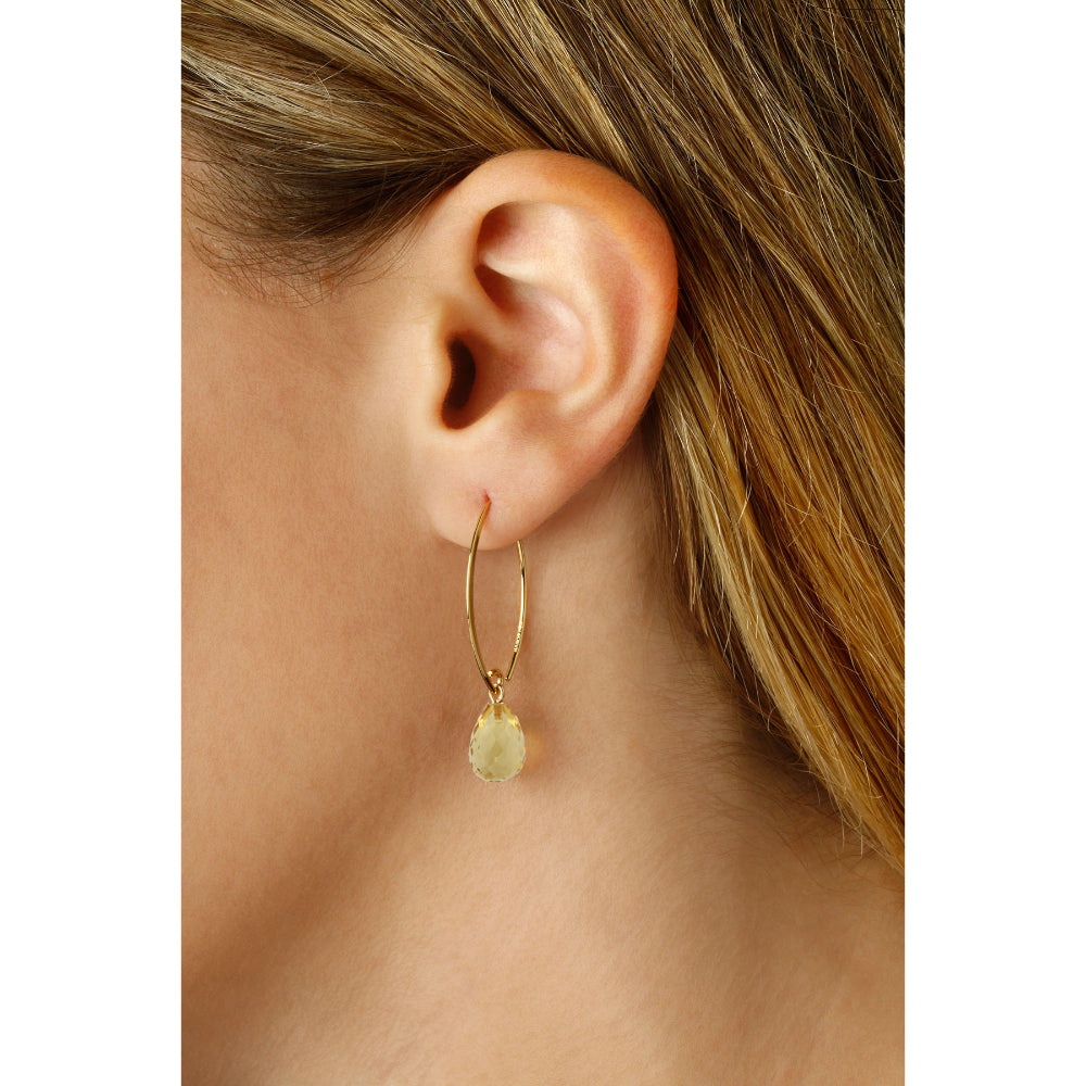 Close-up of an ear wearing a gold hoop earring with a green gemstone.