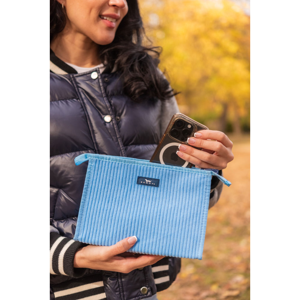 Person holding a blue textured pouch with a phone in an outdoor setting