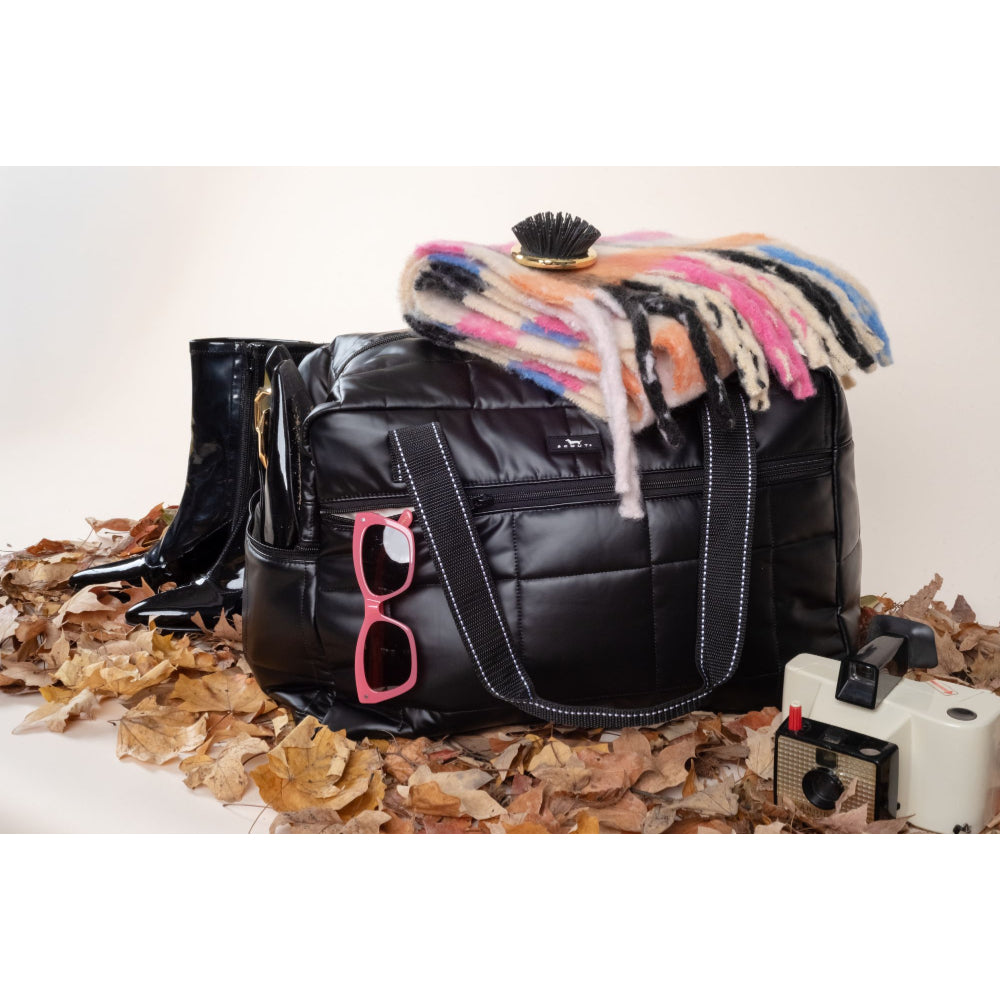 Black quilted handbag with pink sunglasses, colorful scarf, and vintage camera on a textured surface.