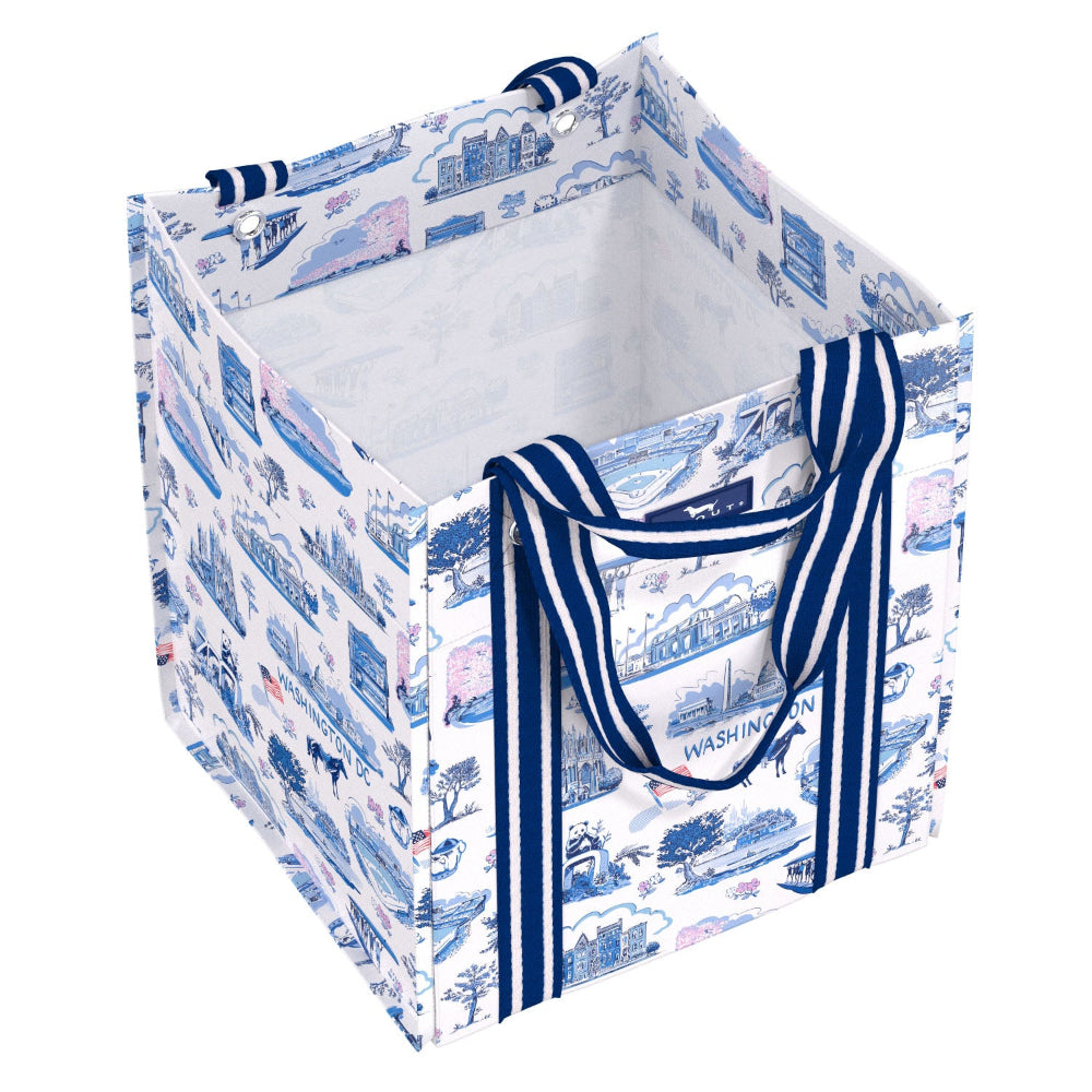 A square fabric storage bin with a white background and a blue toile-style landscape print, featuring thick navy and white striped handles.