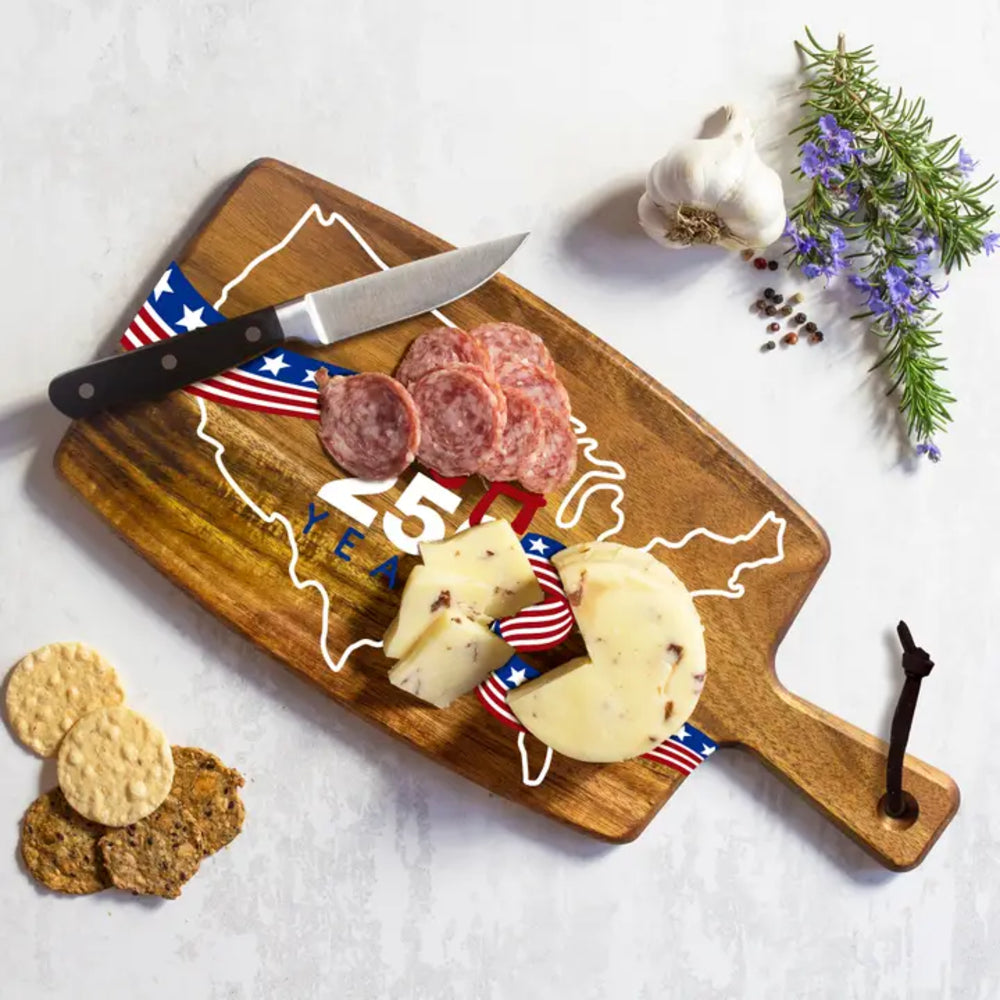 Wooden cutting board with USA 250th with charcuterie display including salami, cheese, crackers, and a knife on a white background.