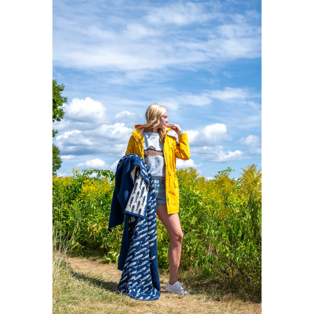 Person holding a blue patterned blanket in a field with a blue sky.