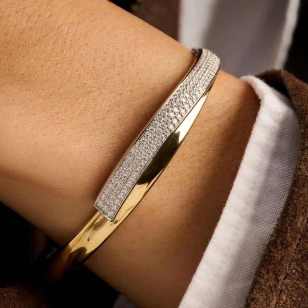 A close-up of a two toned bangle bracelet with a rectangular pavé-set stone twist section worn on a wrist,