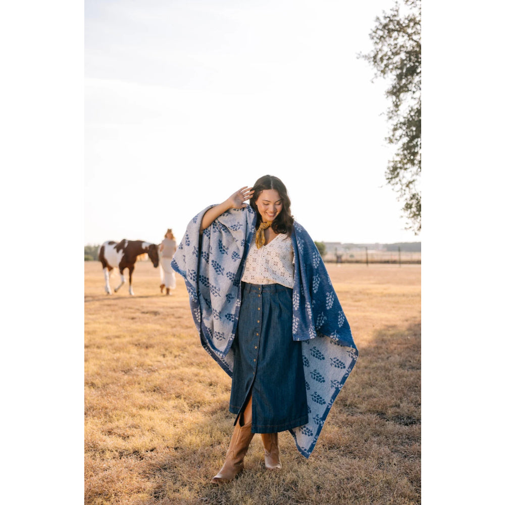 A woman wearing a lightweight blanket around her with blue colors and white floral patterns in an outside background.