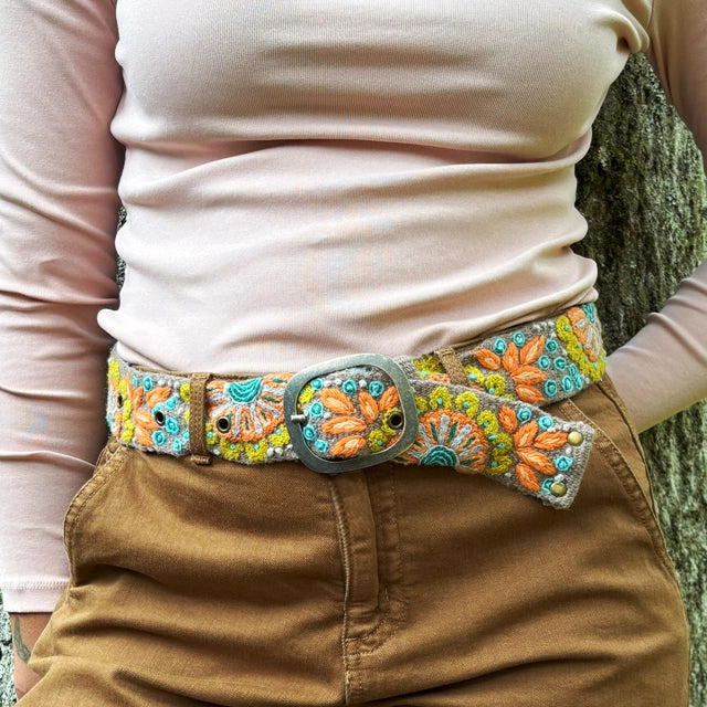 Person wearing a beige shirt and brown pants with an ornate belt featuring floral patterns.