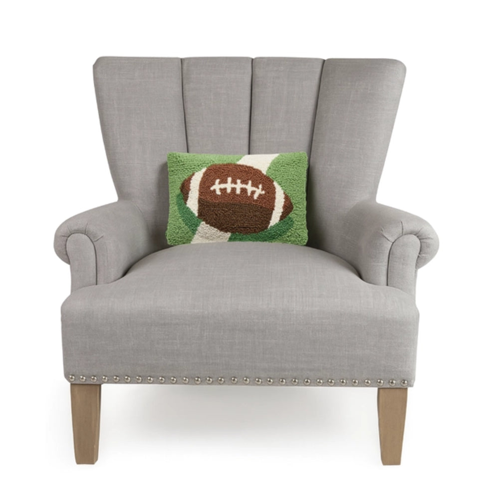 A light gray upholstered wingback armchair with wooden legs and nailhead trim, styled with a green and brown football throw pillow, shown against a plain white background.