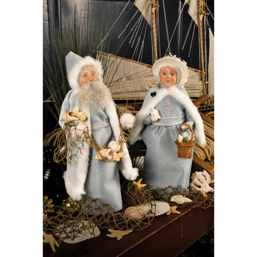 Two decorative figures of the Nautical Santa and Mrs. Claus in front of a sailing ship model with a net, sea shells and starfish.