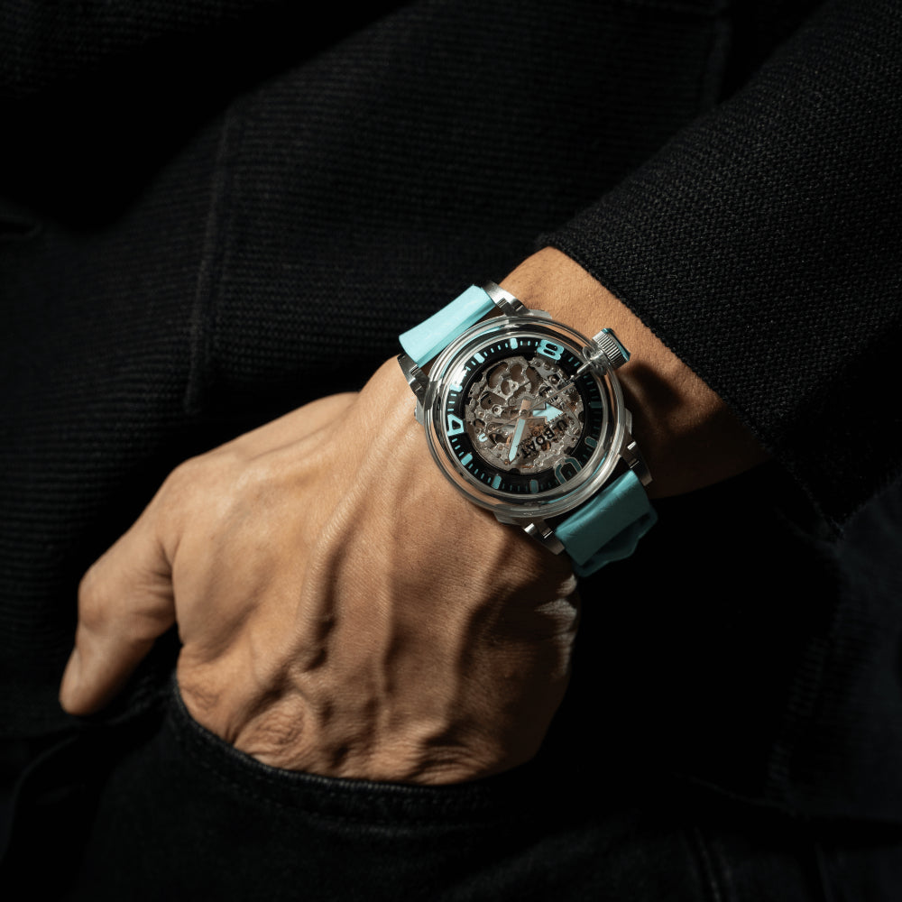 Luxury watch with turquoise strap on a person's wrist against a dark background