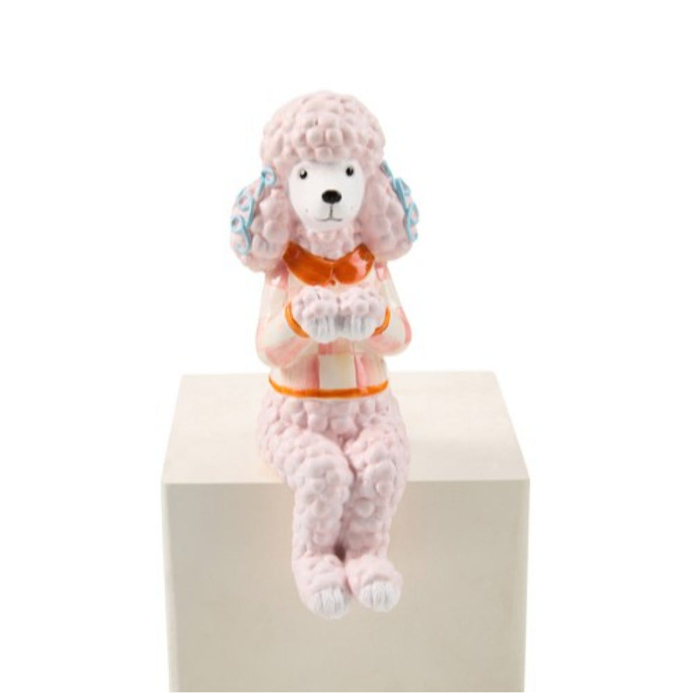 A pink poodle figurine wearing an orange vest and blue-and-white patterned hat, seated on a white display block against a white background.