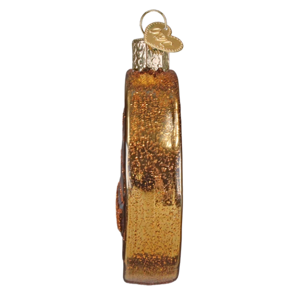 A side view of a penny shaped glass ornament with a textured, glittery amber-brown finish and a small gold hanging loop at the top, shown on a plain white background.