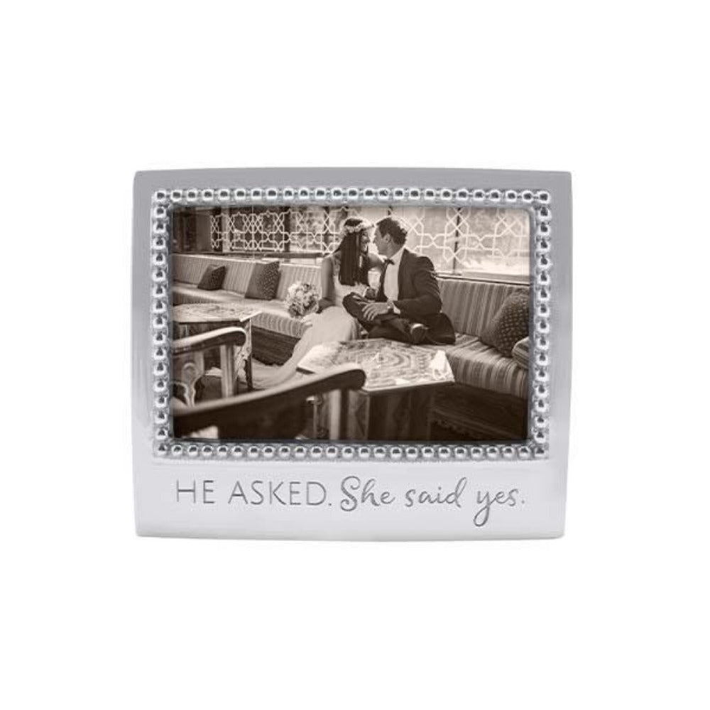 Decorative silver beaded 4x6 photo frame with a couple on a couch and 'He Asked. She Said Yes.' text. On a white backround
