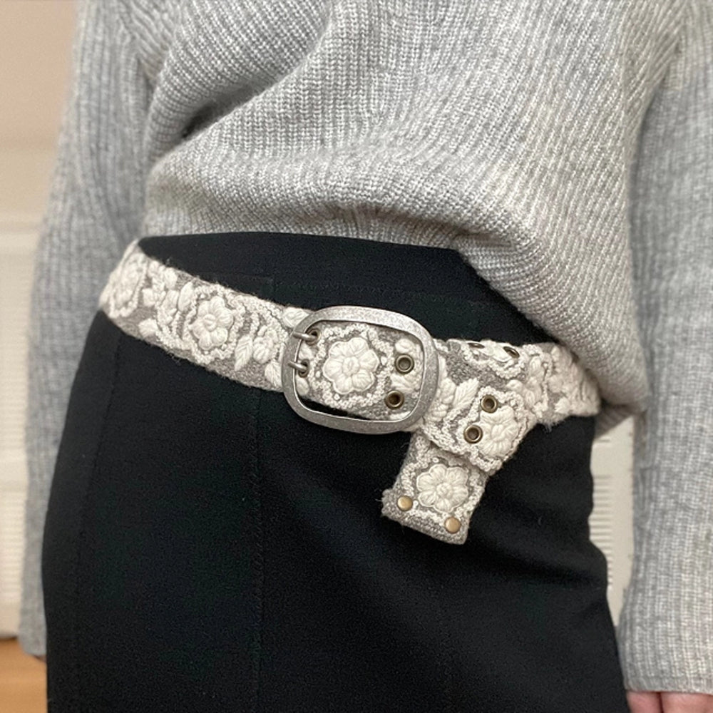 Person wearing a gray sweater and black pants with a decorative belt.