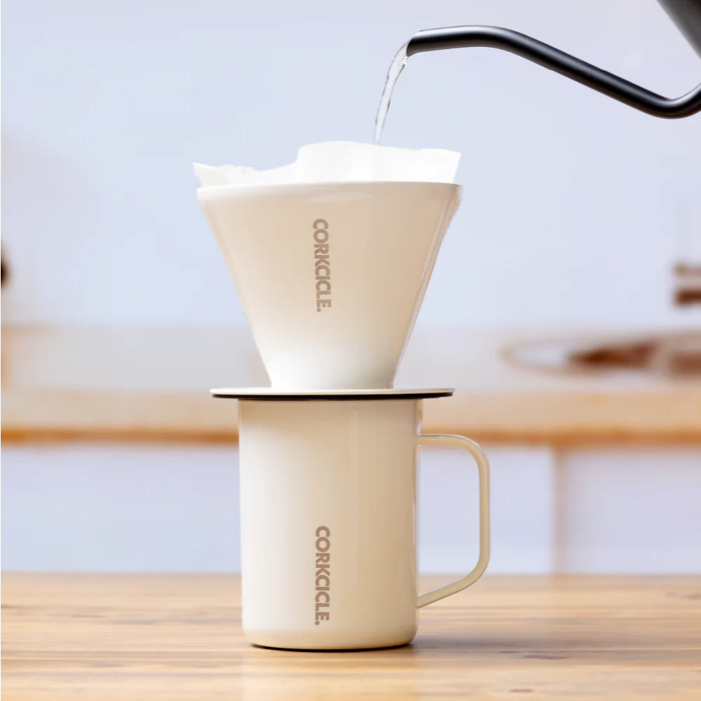 White Corkcicle coffee pour-over being used to pour coffee into a mug on a wooden surface.