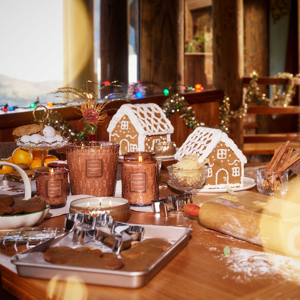 Wooden table with gingerbread houses, baking tools, with candles and a festive background.