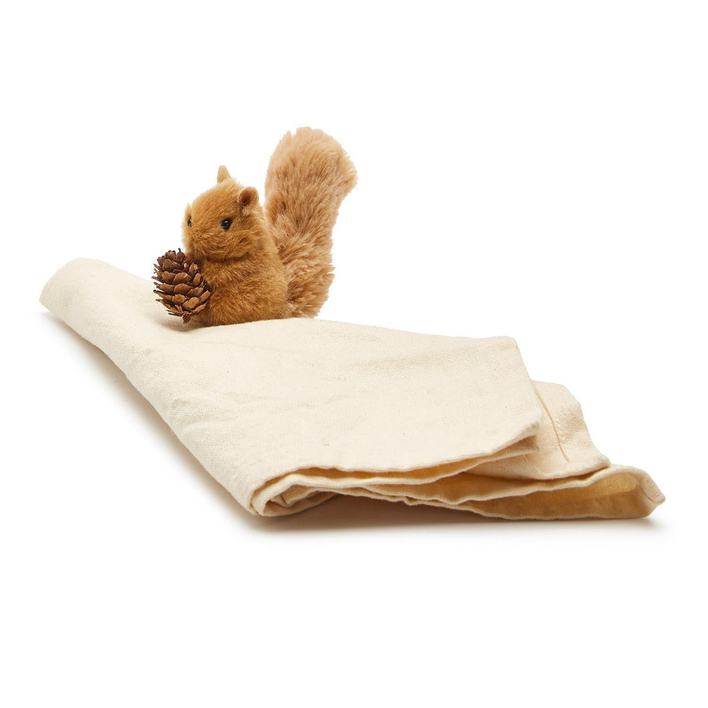 Plush squirrel toy with a pine cone on a folded beige blanket against a white background