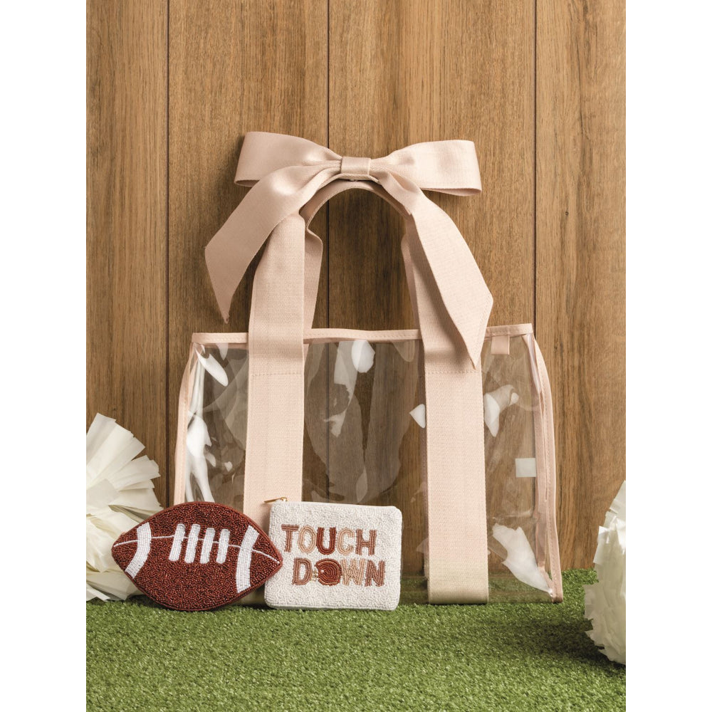 Clear gift bag with pink ribbon, football-shaped item, and 'Touchdown' sign on grass against wooden background.