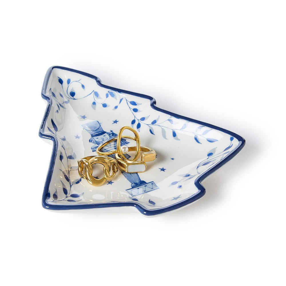 Decorative white dish shaped like a tree with a blue nutcreacker holding gold rings on a white backgroun.