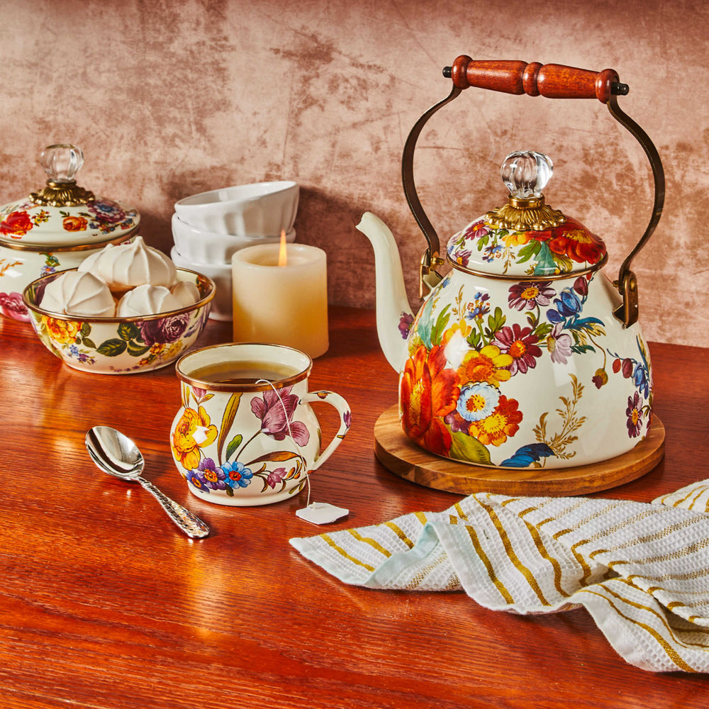 White with colorful floral patterned mug with a yellow rose on a brown wood table with a simular patterned tea kettle with other items