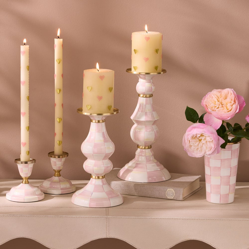 Decorative candles and candlesticks with a vase of flowers on a beige surface.