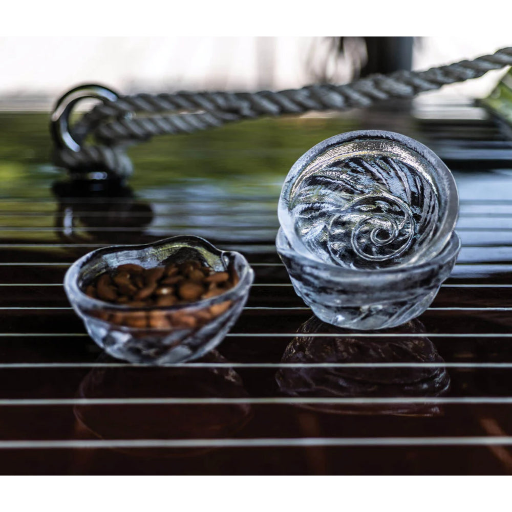 Two glass bowls with coffee beans on a brown reflective surface.