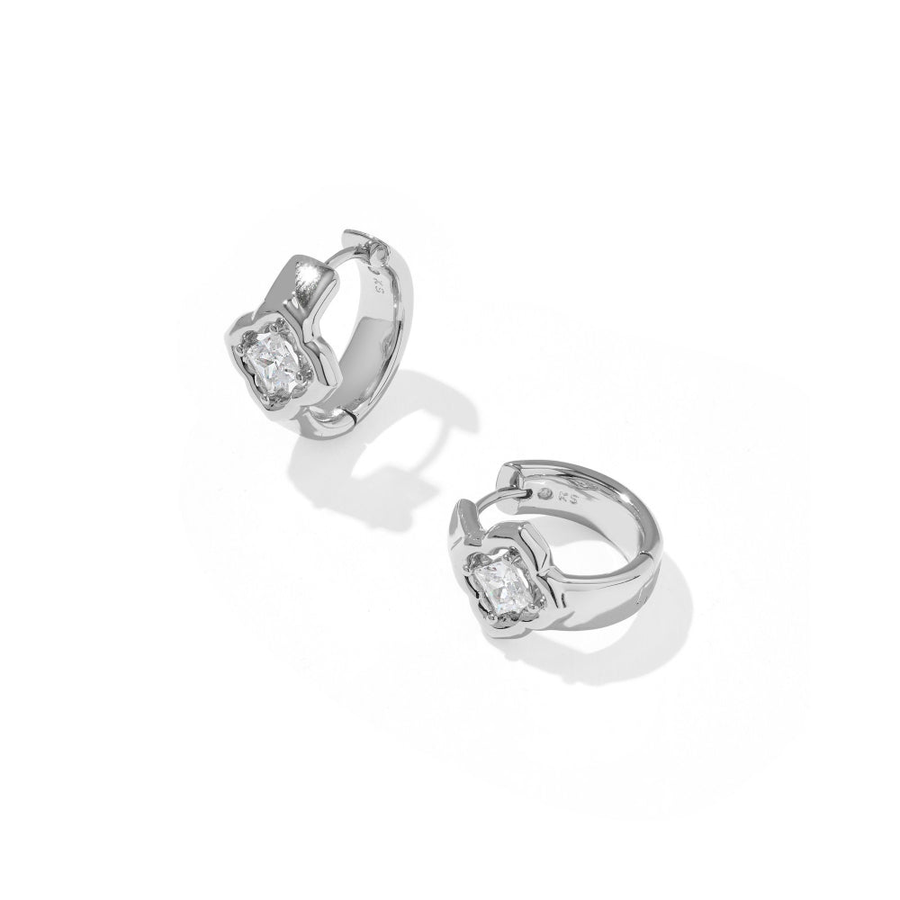 A pair of silver huggie hoop earrings with a central bezel-set clear gemstone, displayed on a clean white background with soft shadows.
