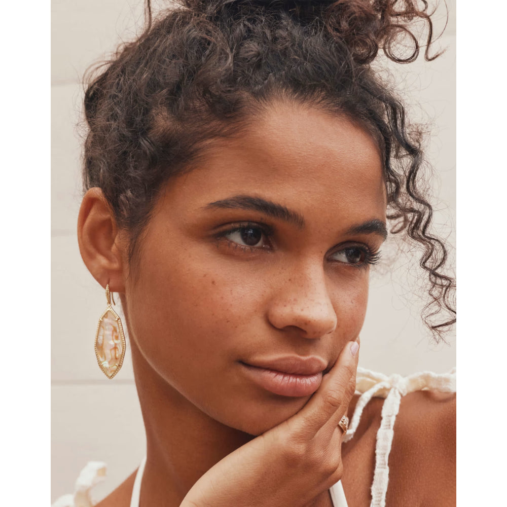 Close-up of a woman with curly hair wearing gold earrings and a ring.
