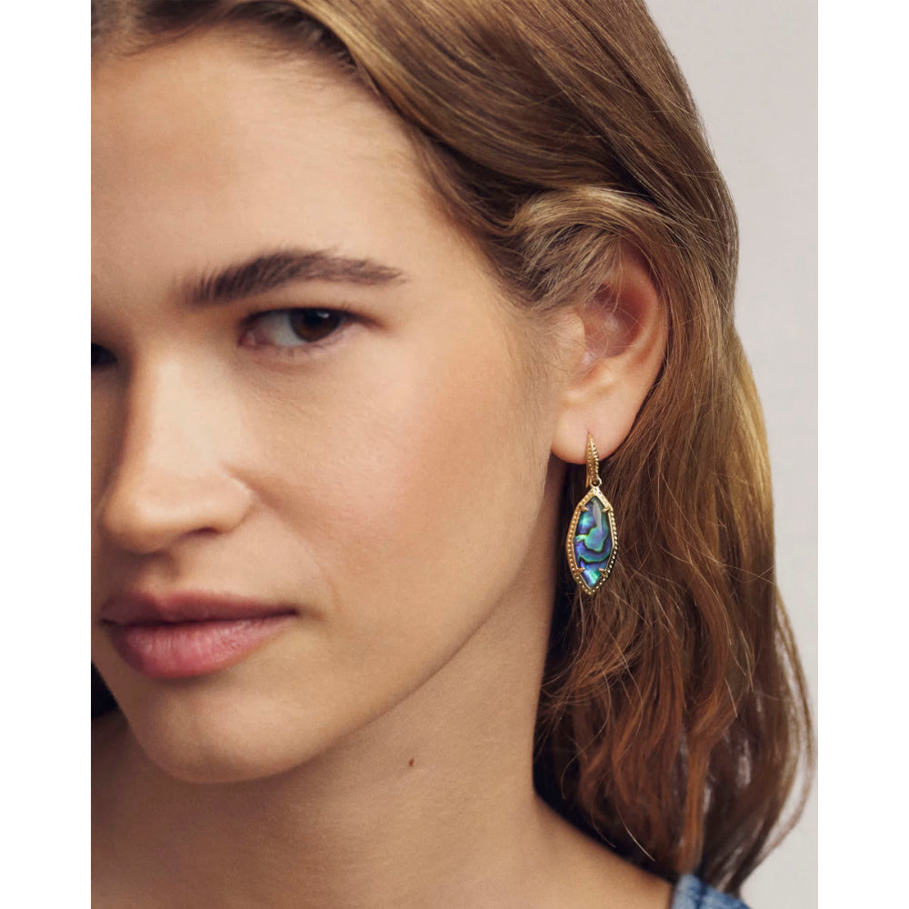 Close-up of a woman wearing a gold earring with a blue gemstone.