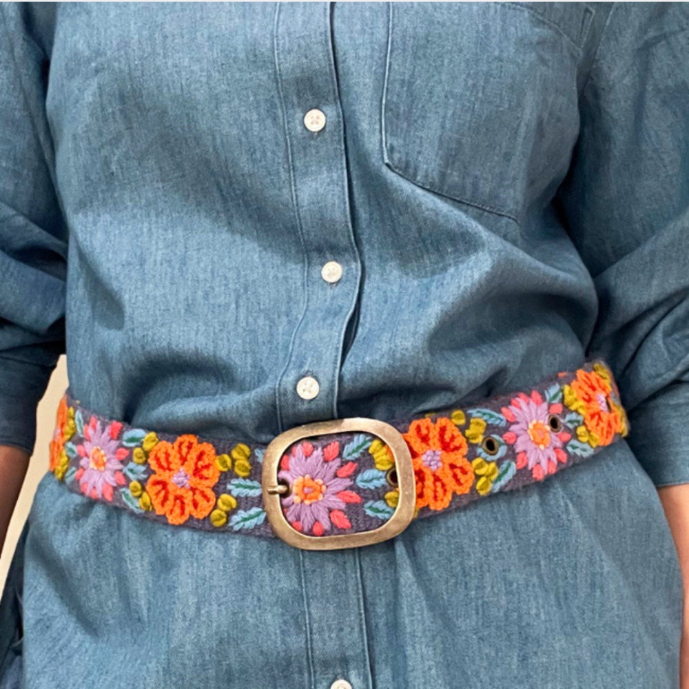 Person wearing A colorful embroidered wool belt with a floral pattern and a metal buckle.