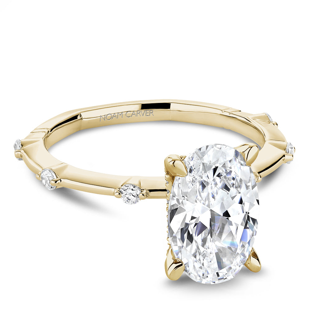 Gold Noam Carver ring with an oval diamond center and round diamond shank accents on a white background