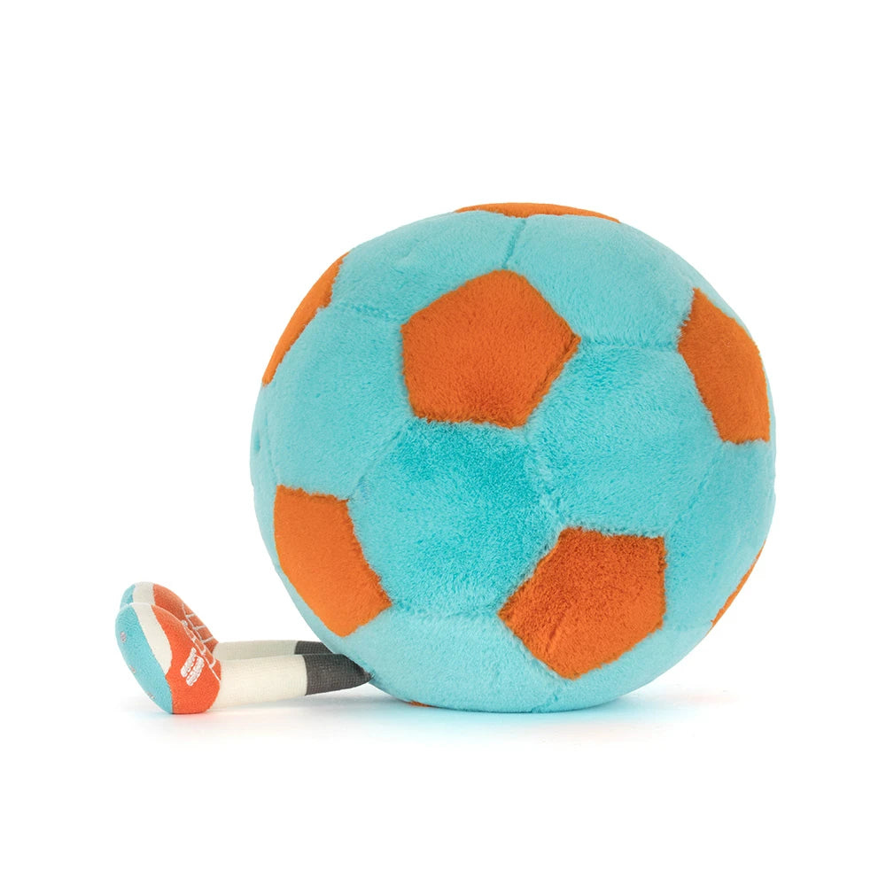 A side photo of a teal and orange Jellycat Amuseables Soccer Ball push toy with a smiling face and white legs on a white background.