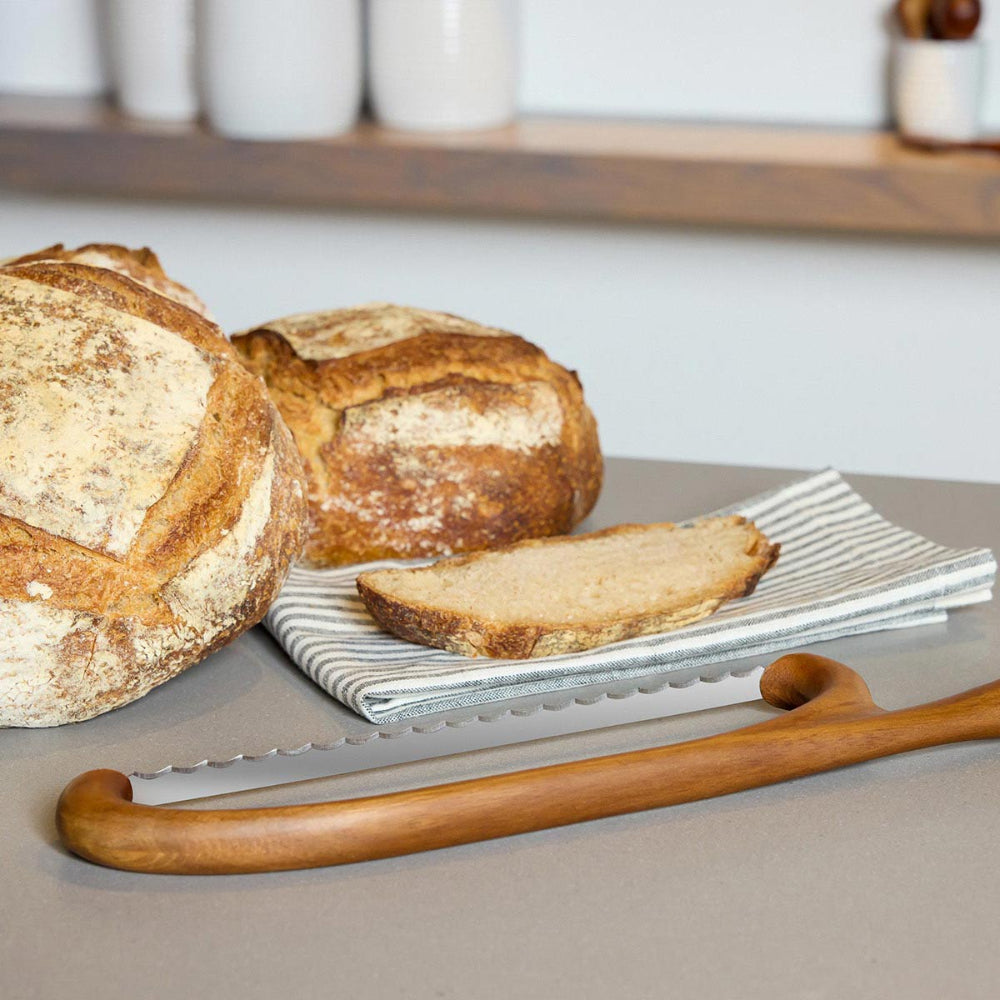 Two loaves of bread with a sliced piece on a napkin, accompanied by a bread knife on a neutral background.