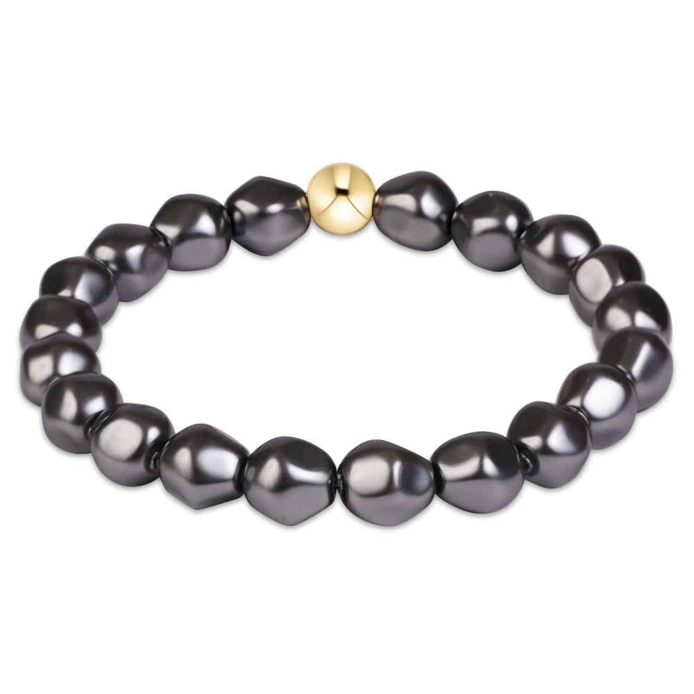 A beaded stretch bracelet featuring irregular, glossy dark gray freshwater pearls and a single central gold spacer bead, shown on a plain white background.