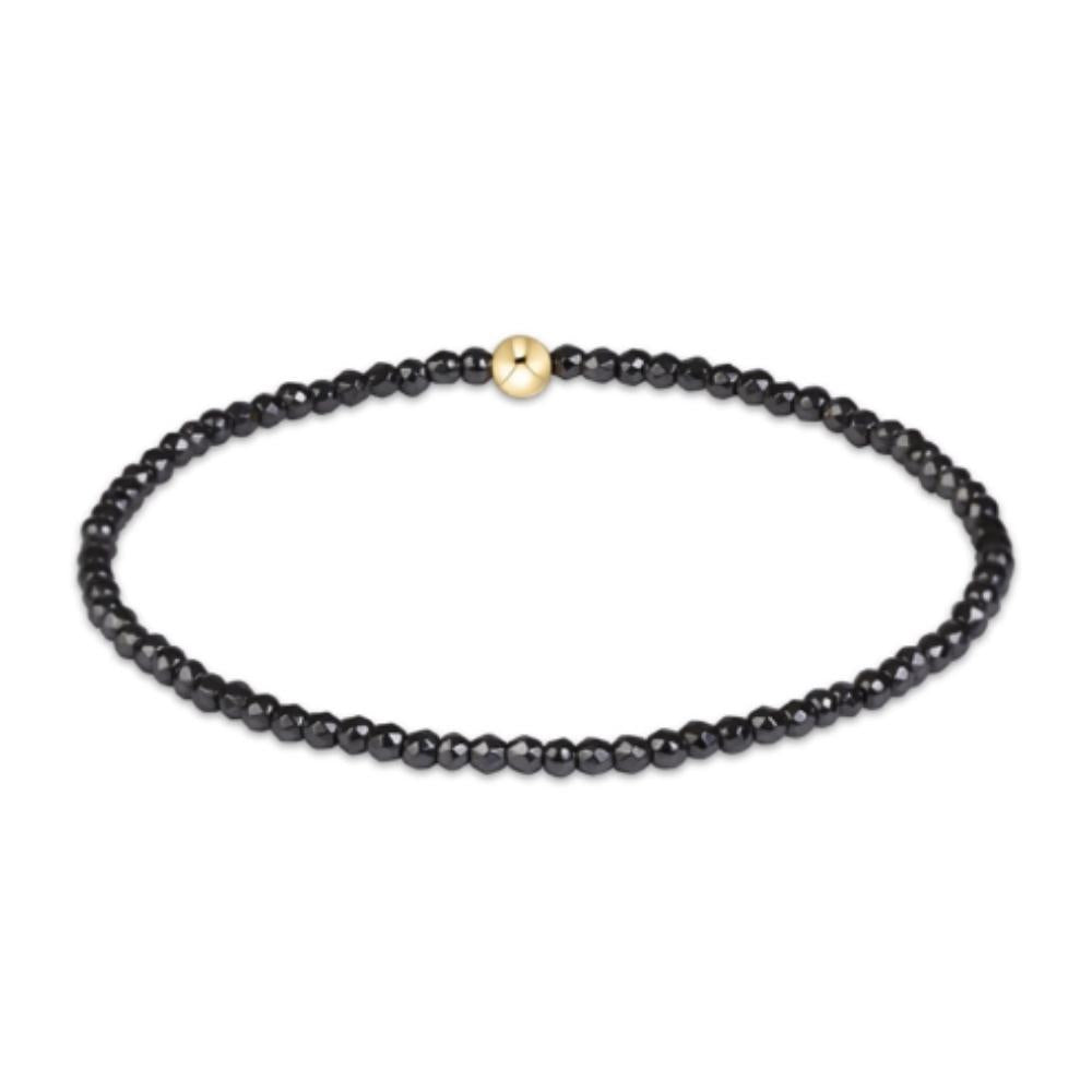 A beaded bracelet made of small faceted black beads with a single polished gold round bead clasp, shown on a plain white background.