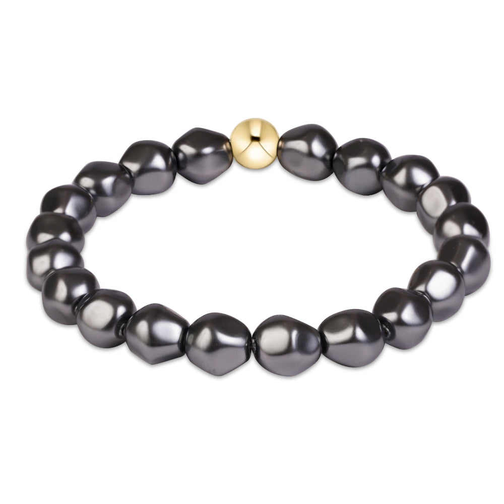 A beaded stretch bracelet featuring irregular, glossy dark gray freshwater pearls and a single central gold spacer bead, shown on a plain white background.