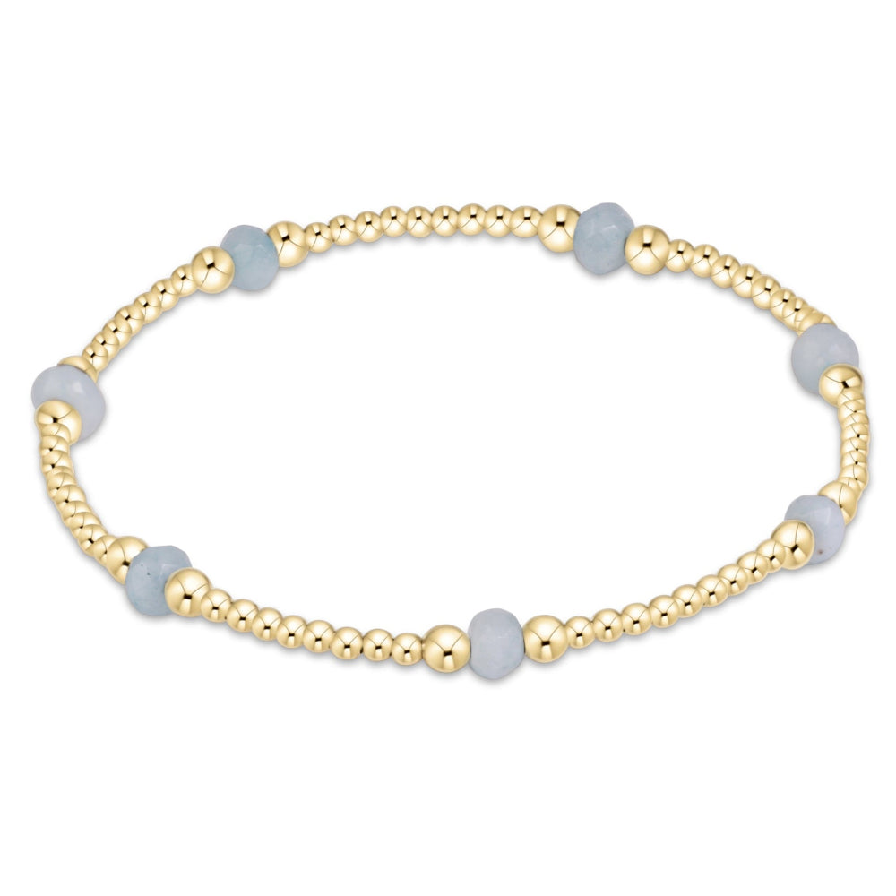 A gold beaded stretch bracelet featuring alternating smooth, light blue-gray round beads and polished gold spacer beads, shown on a plain white background.