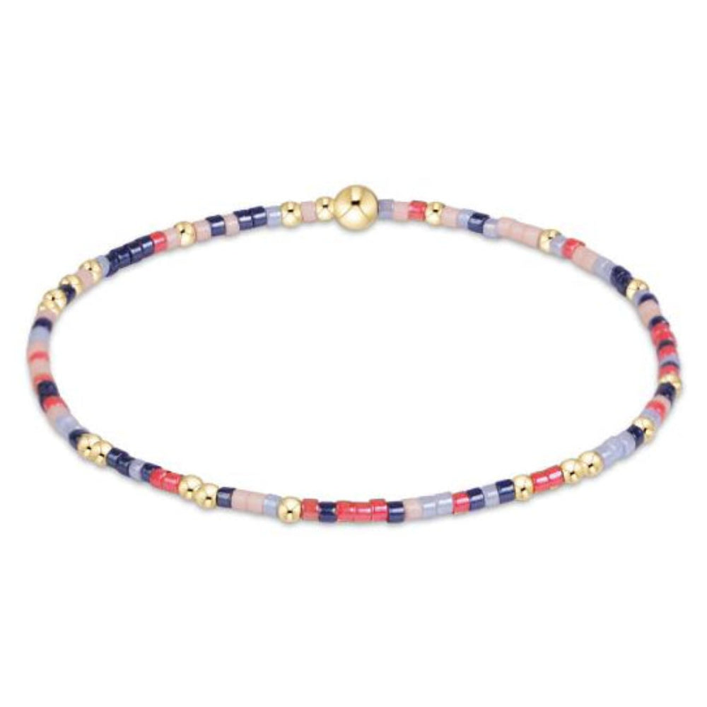 A delicate beaded bracelet with alternating segments of navy blue, red, light pink, and pale lavender beads, accented by small gold spacer beads and a central gold sphere bead, shown on a plain white background.