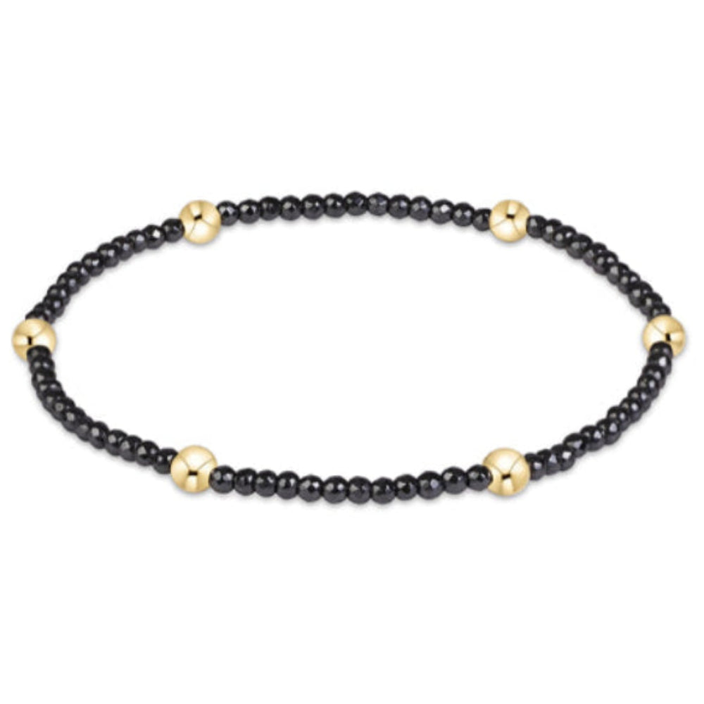A beaded stretch bracelet featuring small black faceted beads and five polished gold round spacer beads, displayed on a clean white background.