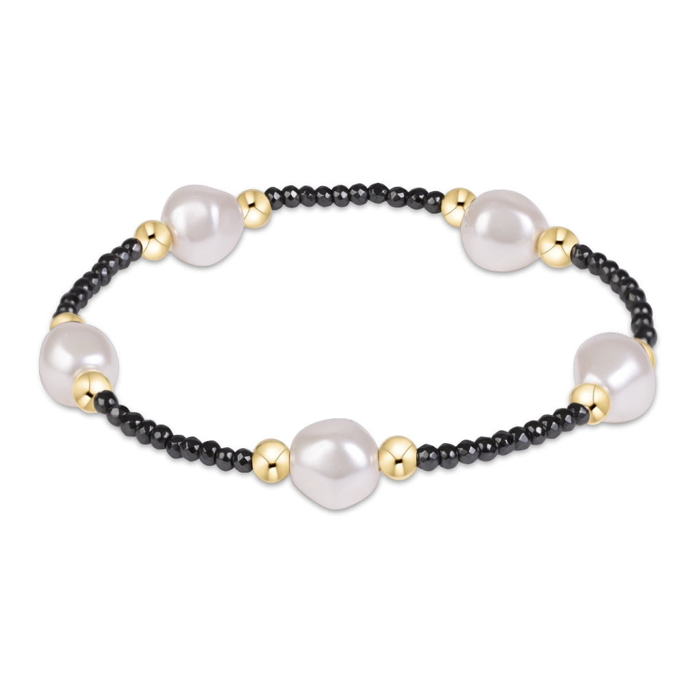 A beaded bracelet featuring large, irregular white freshwater pearls separated by small black beads and polished gold spacer beads, shown on a plain white background.