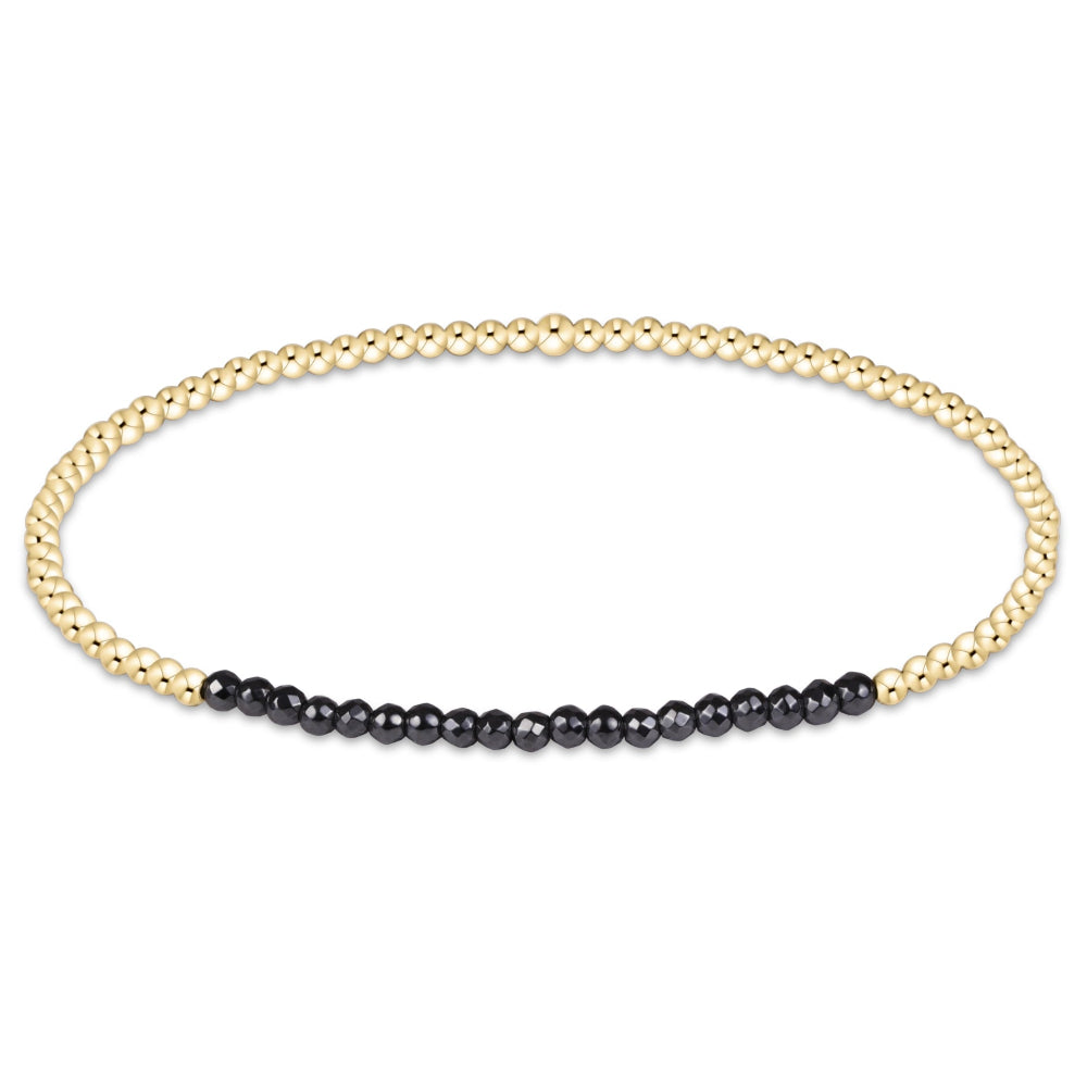 A delicate gold chain bracelet with a short segment of small black beads on one side, displayed against a solid white background.