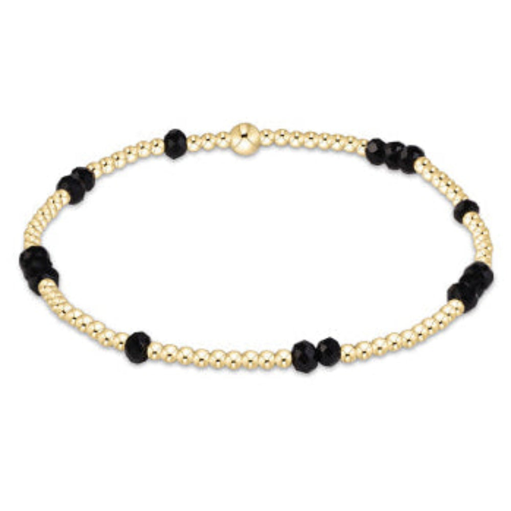 A delicate beaded bracelet featuring alternating strands of small gold-toned beads and larger matte black faceted beads, with a polished gold clasp at the top, shown on a plain white background.