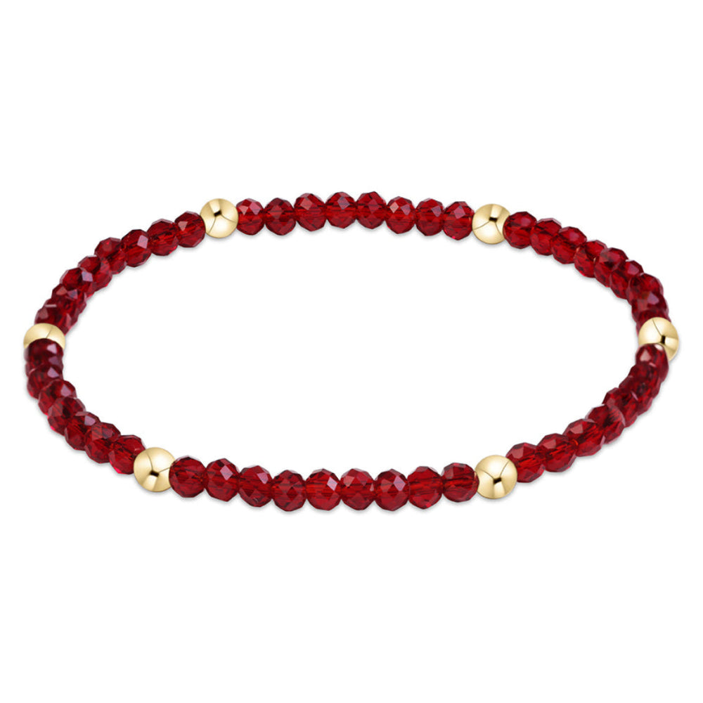 A beaded stretch bracelet featuring faceted deep red beads and small polished gold spacer beads, displayed on a clean white background.