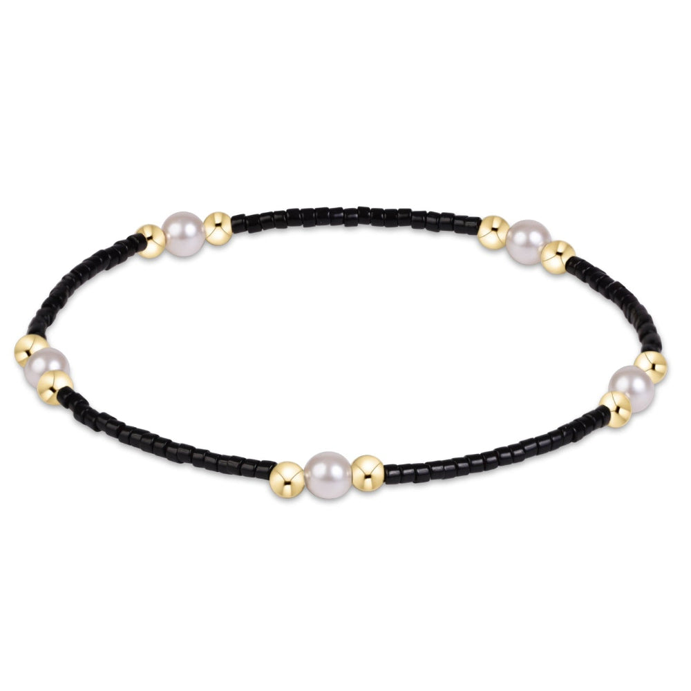 A delicate black beaded bracelet with alternating white freshwater pearls and polished gold spacer beads, displayed on a clean white background.