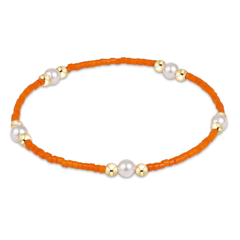 An orange beaded bracelet with alternating white pearls and gold spacer beads, arranged in a circular shape on a plain white background.