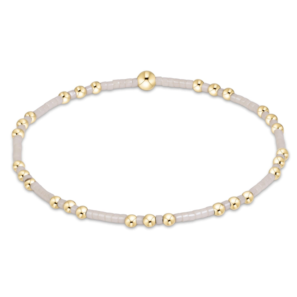 A delicate beaded bracelet featuring small white beads separated by tiny gold metallic beads, with a polished gold center accent, shown on a plain white background.